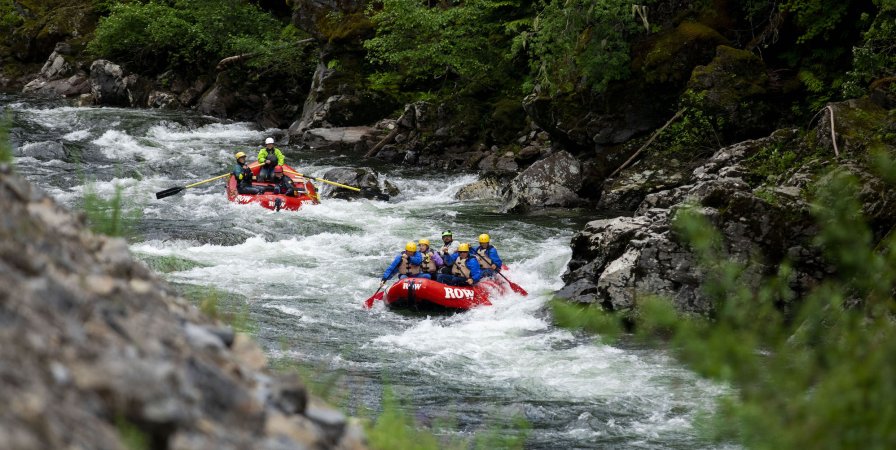 Two red rafts with paddlers moving downstream through a narrow chute rapid 