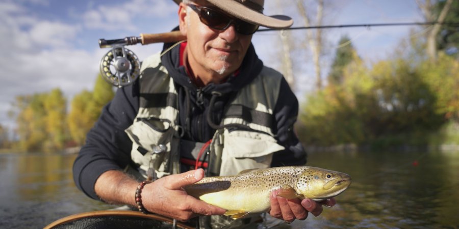 Angler holding a cutthroat trout above a net in a shallow Idaho river on a guided fly fishing tour.
