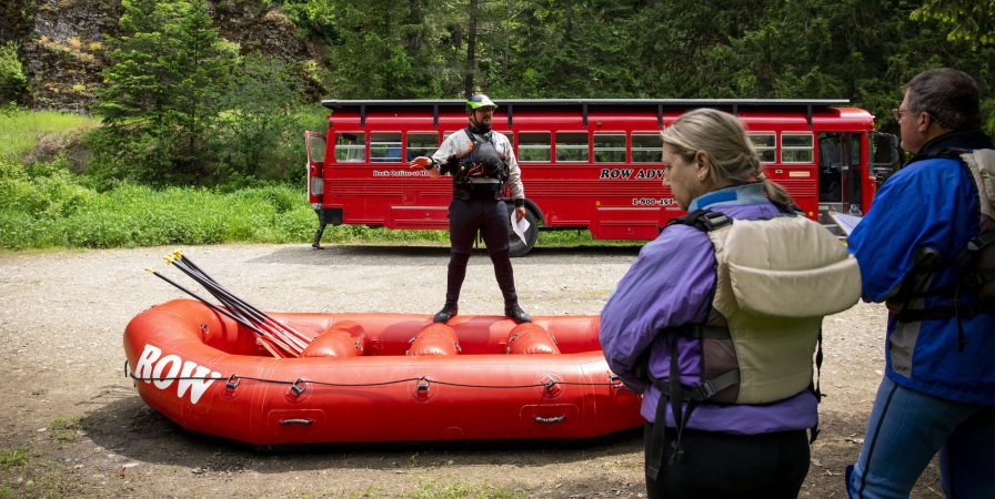 A guide standing in front of a red bus with a red raft discussing rafting safety