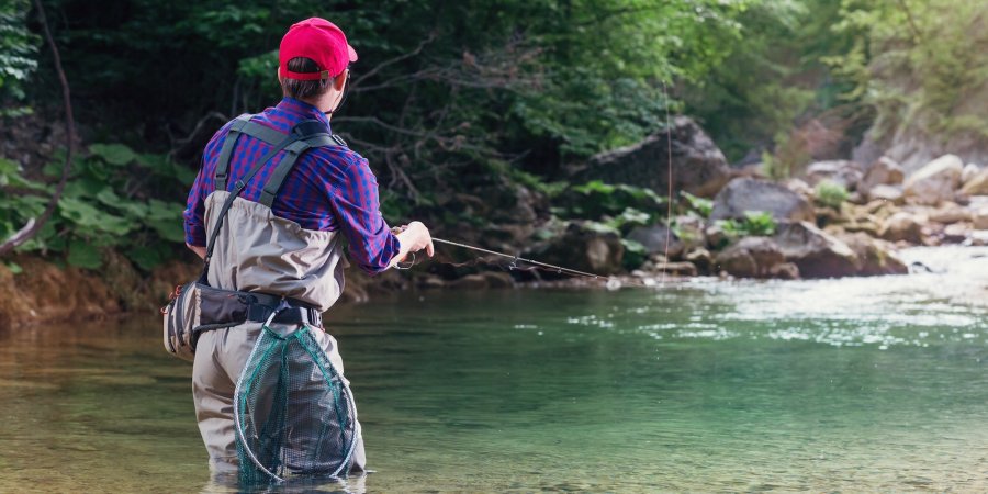 Fly fisherman standing knee-deep in the St. Joe River in Idaho, casting into a calm, clear pool.