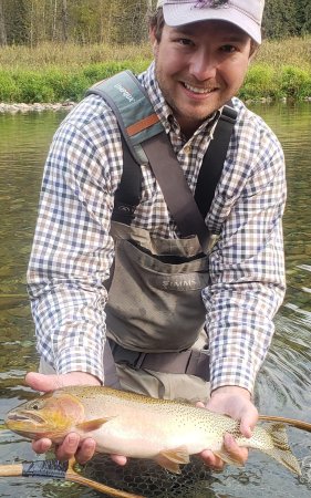Angler standing in a calm Idaho river holding a cutthroat trout above his net during a guided fly fishing trip.