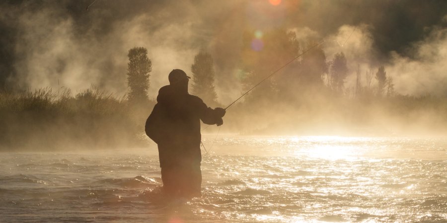 Angler silhouetted in the early morning mist while fly fishing on the St. Joe River in Idaho.