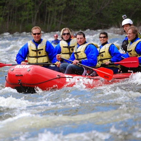 Group of paddlers in blue splash jackets and yellow life jackets in a red raft on the Moyie River