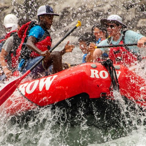 Group paddling through splashy whitewater rapids in a red raft.
